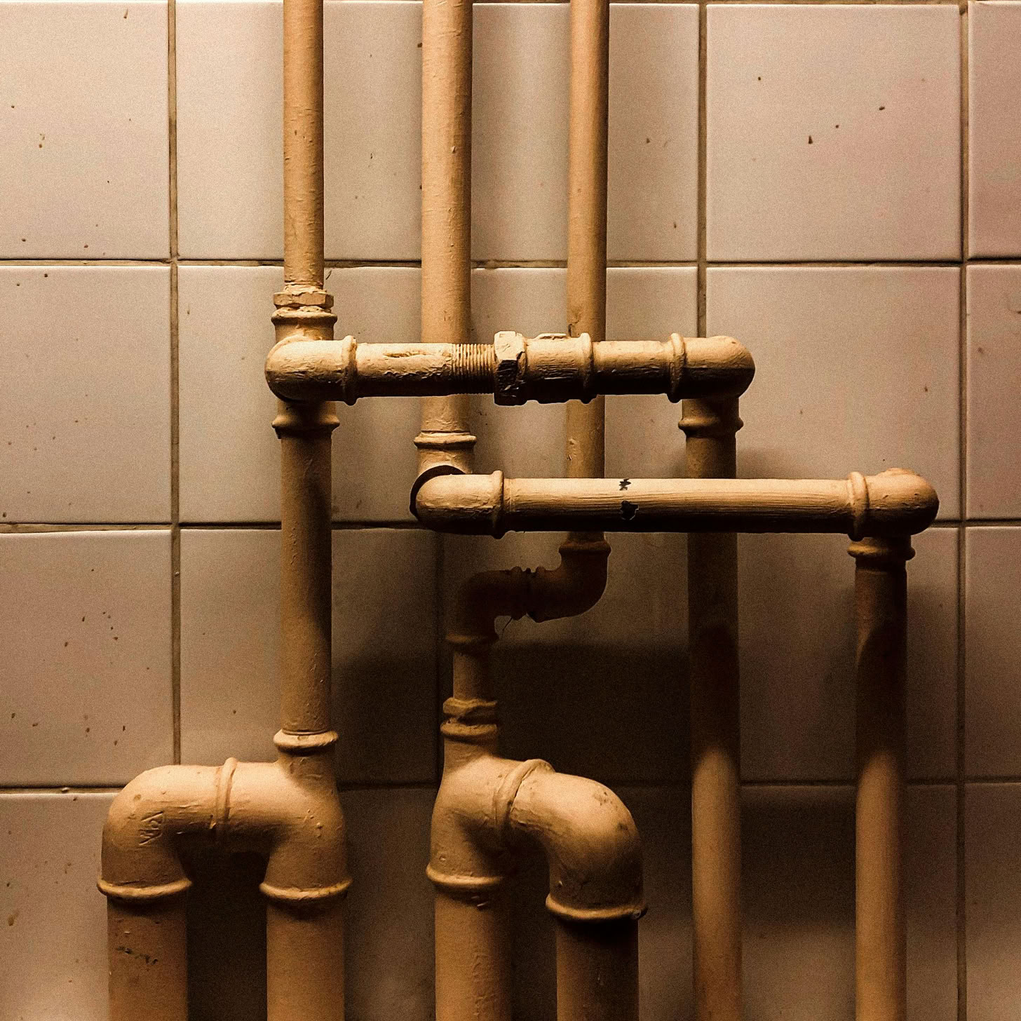 An artistic capture of vertical industrial pipes against a tiled wall, showcasing geometry.