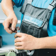 Close-up of a plumber in blue uniform working on a pipe repair with a wrench.